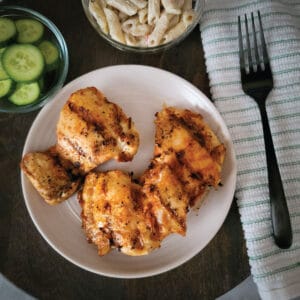 Boneless chicken thighs on a plate ready to eat along with some pasta salad and cucumbers on the side.