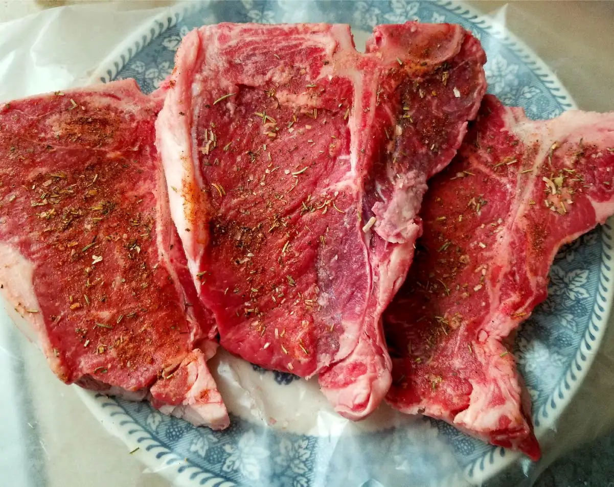 Steaks sitting out on a plate with dry rub on them before grilling.