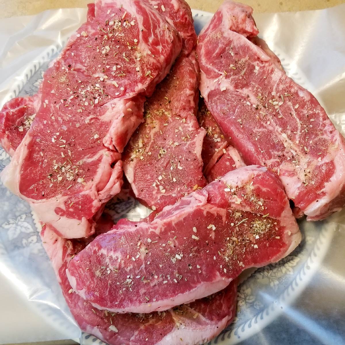 Steaks coated with dry rub sitting on a plate resting before grilling.