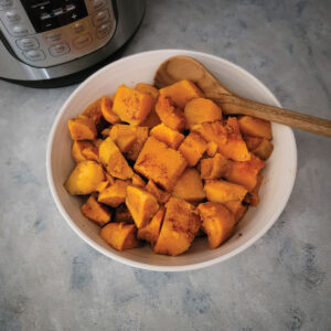 Cooked sweet potatoes and butternut squash with cinnamon and nutmeg on top in a serving bowl.