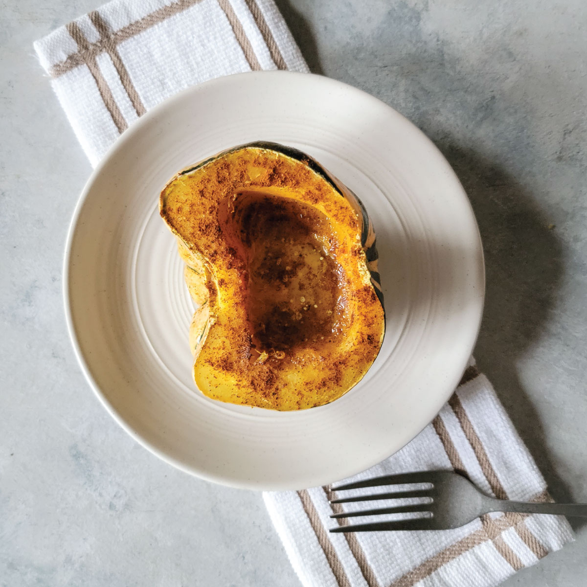 Half of a roasted sweet dumpling squash on a serving plate with seasoning and melted butter.