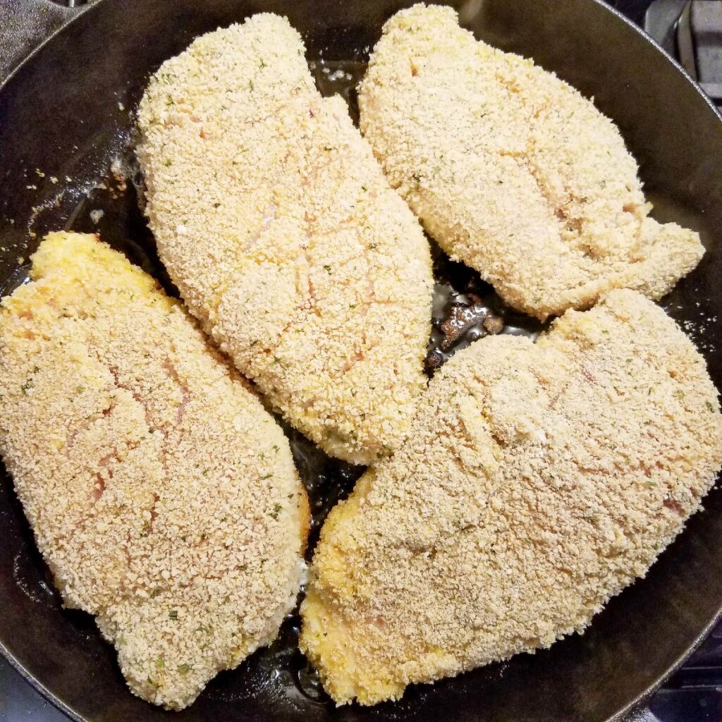 Chicken breasts breaded and frying in the cast iron pan
