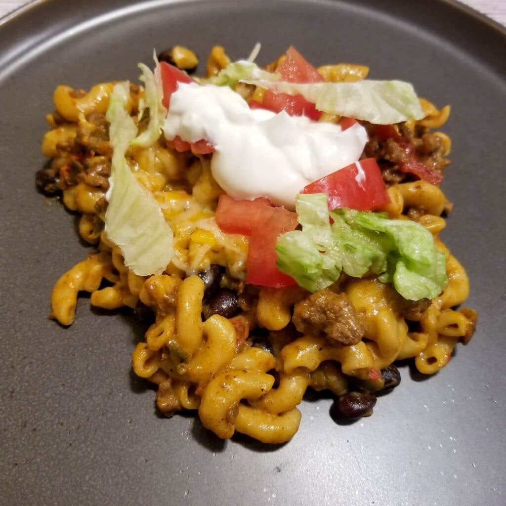 Taco pasta on a plate with sour cream, lettuce and tomato