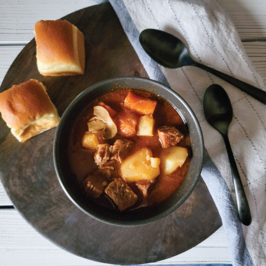 Beef stew in the bowl with a piece of beef on the spoon.