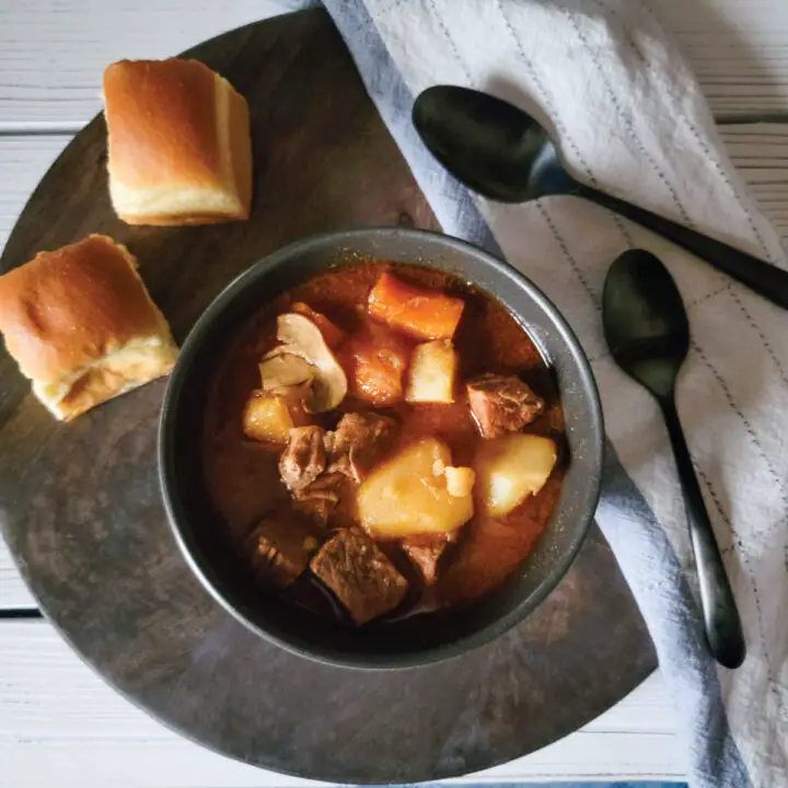 beef stew in a bowl ready to be served with 2 dinner rolls