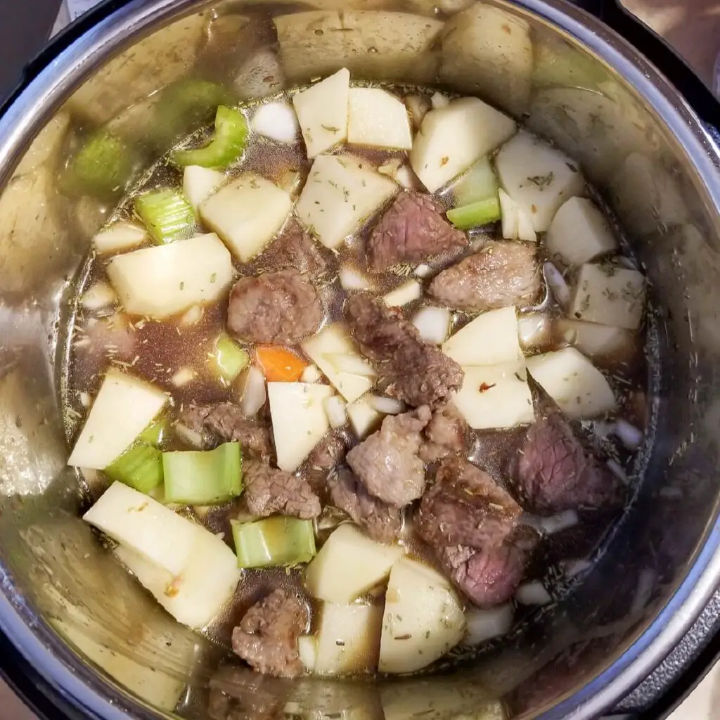 beef and vegetables in the Instant Pot with broth ready to pressure cook.