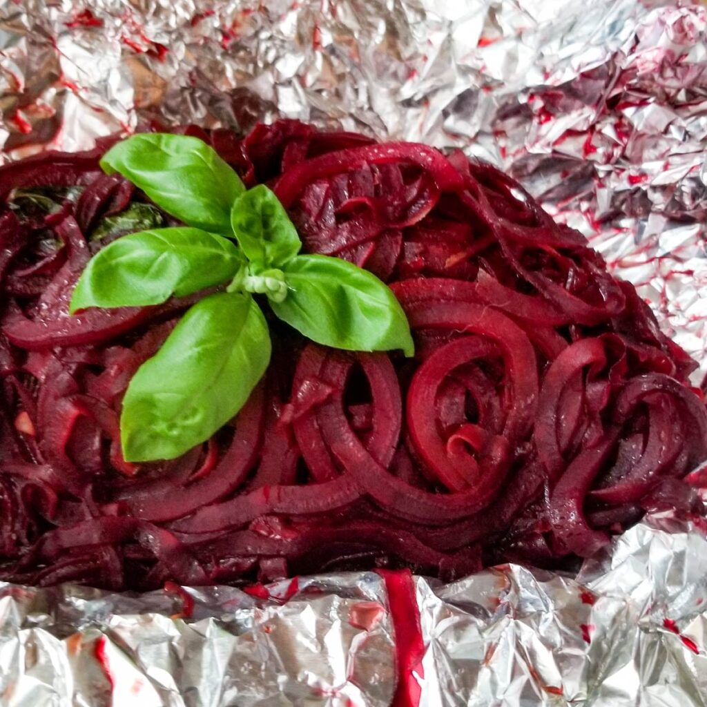 Cooked spiralized beets in the open foil packet with basil on top as a garnish