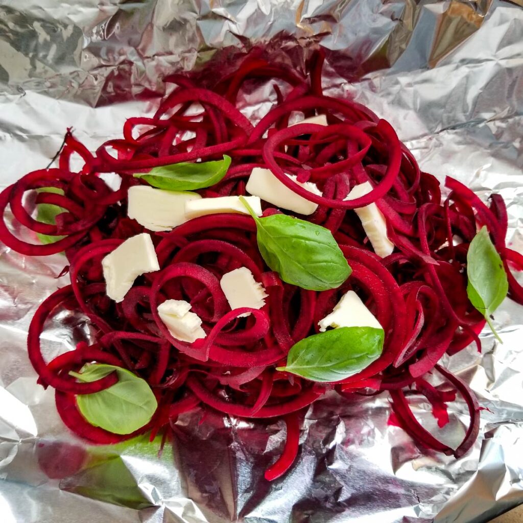 Spiralized beets in a pile on top of foil with thin slices of butter and fresh basil leaves on top.