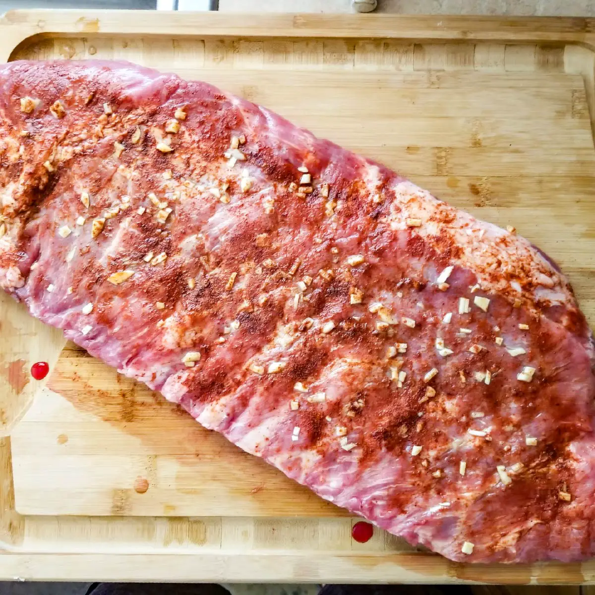 Rack of ribs sitting out on a cutting board with seasoning ready to go on grill.