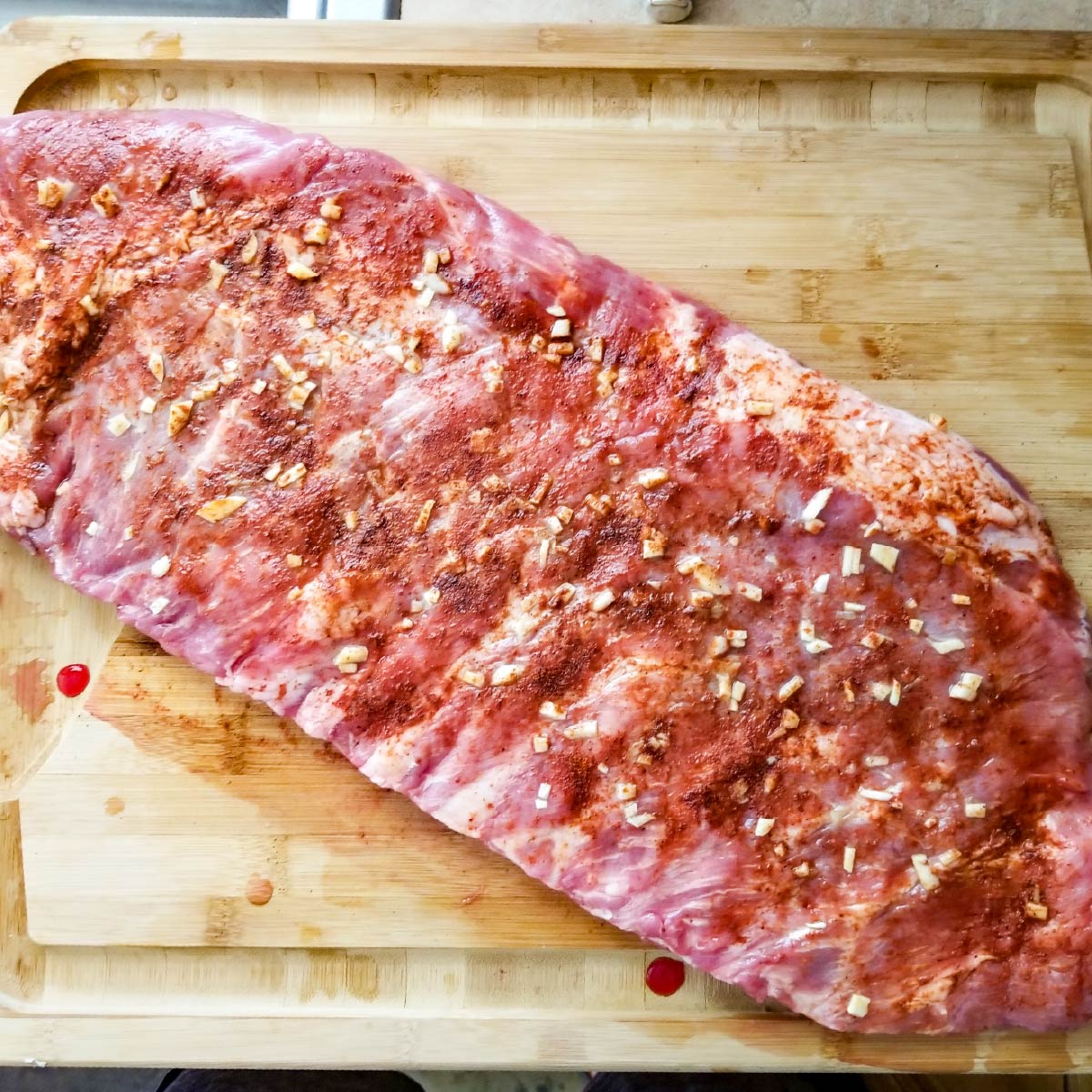 Rack of ribs sitting out on a cutting board with seasoning ready to go on grill.