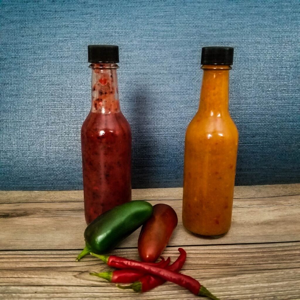 bottled hot sauce in 5 ounce bottles with hot peppers next to them