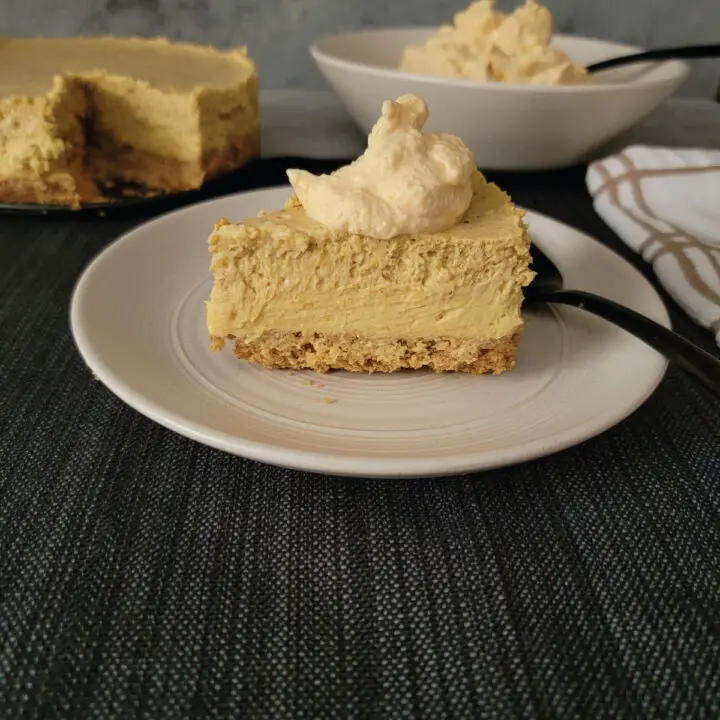 Pumpkin cheesecake on a dessert plate topped with whipped cream ready to eat.