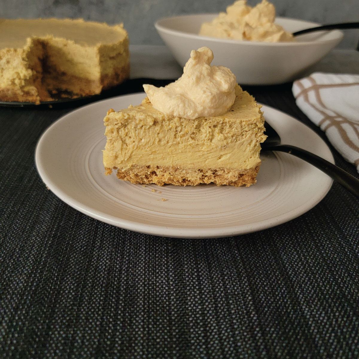 Slice of pumpkin cheesecake on a plate with whipped cream on top.