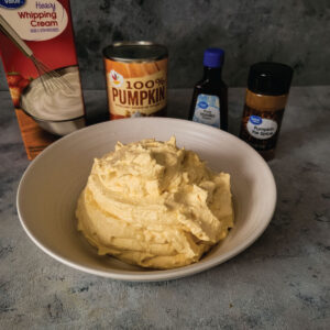Pumpkin whipped cream in a bowl with whipping cream, can of pumpkin, pumpkin pie spice and vanilla extract in the background.