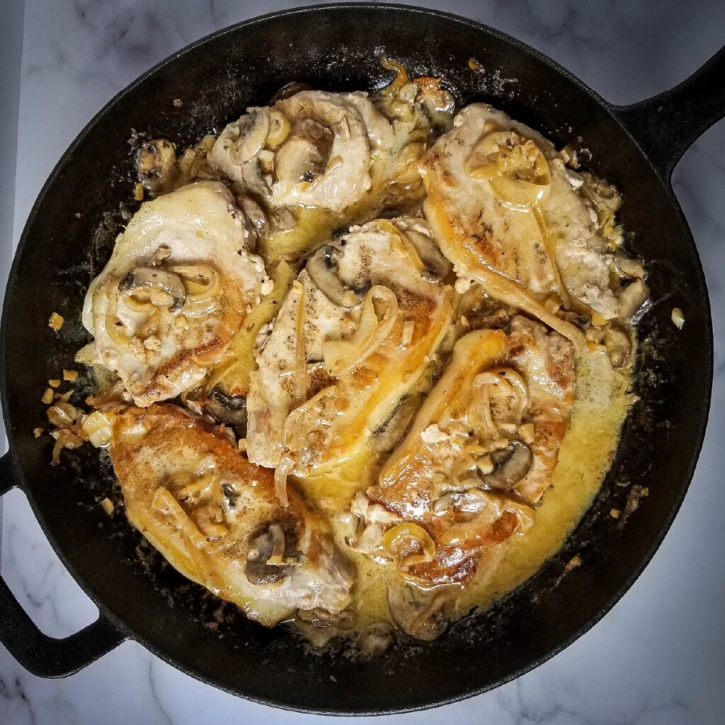 Pork chops in a frying pan with mushrooms and sauce on them ready to be served.