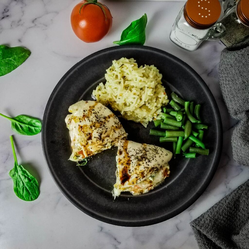 Stuffed chicken on a plate with rice and green beans about to be served.