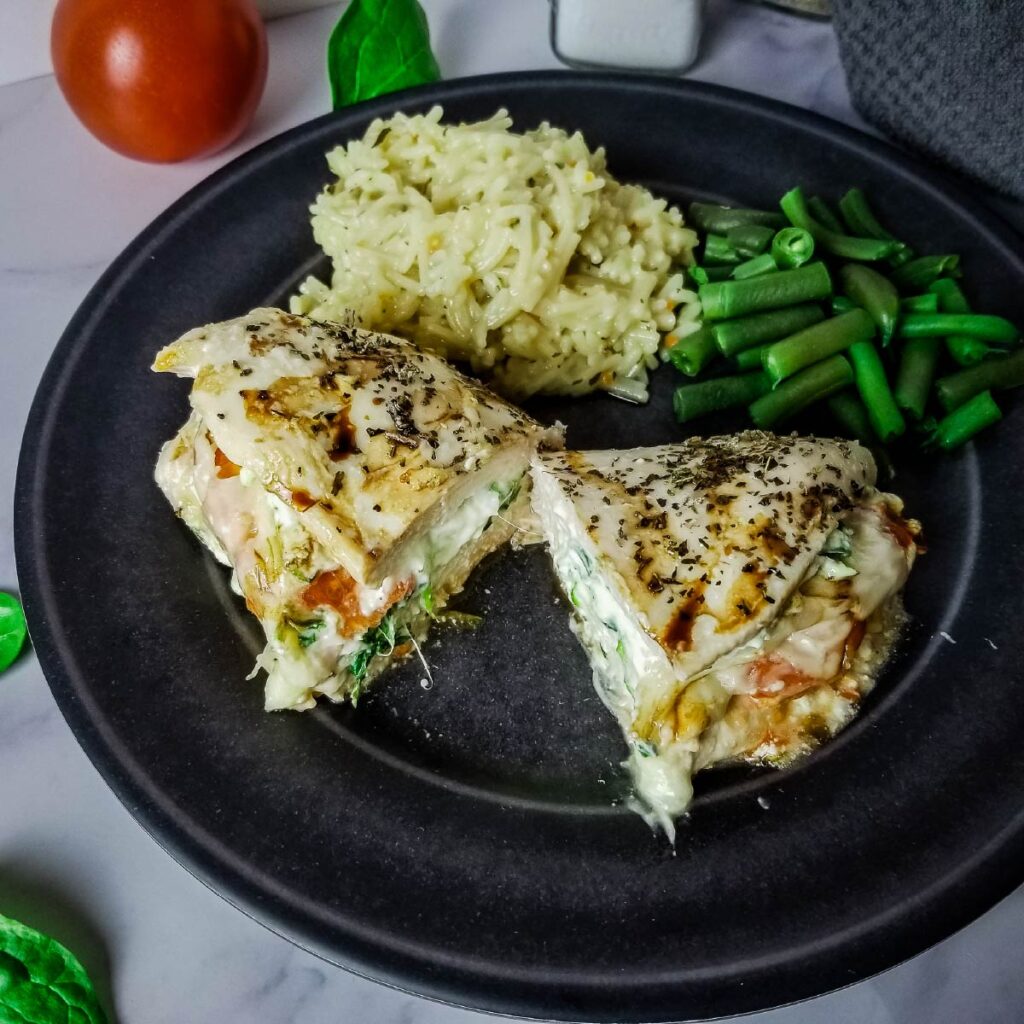 Stuffed chicken breast on a plate cut in half with rice and green beans.