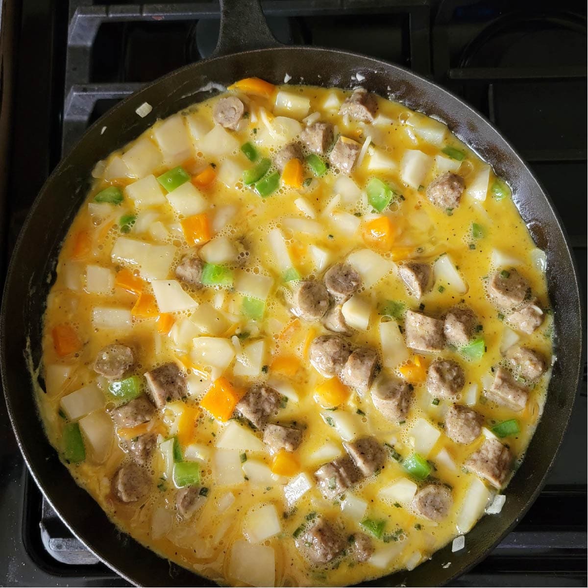 Vegetables, sausage and eggs in cast iron pan getting ready to bake