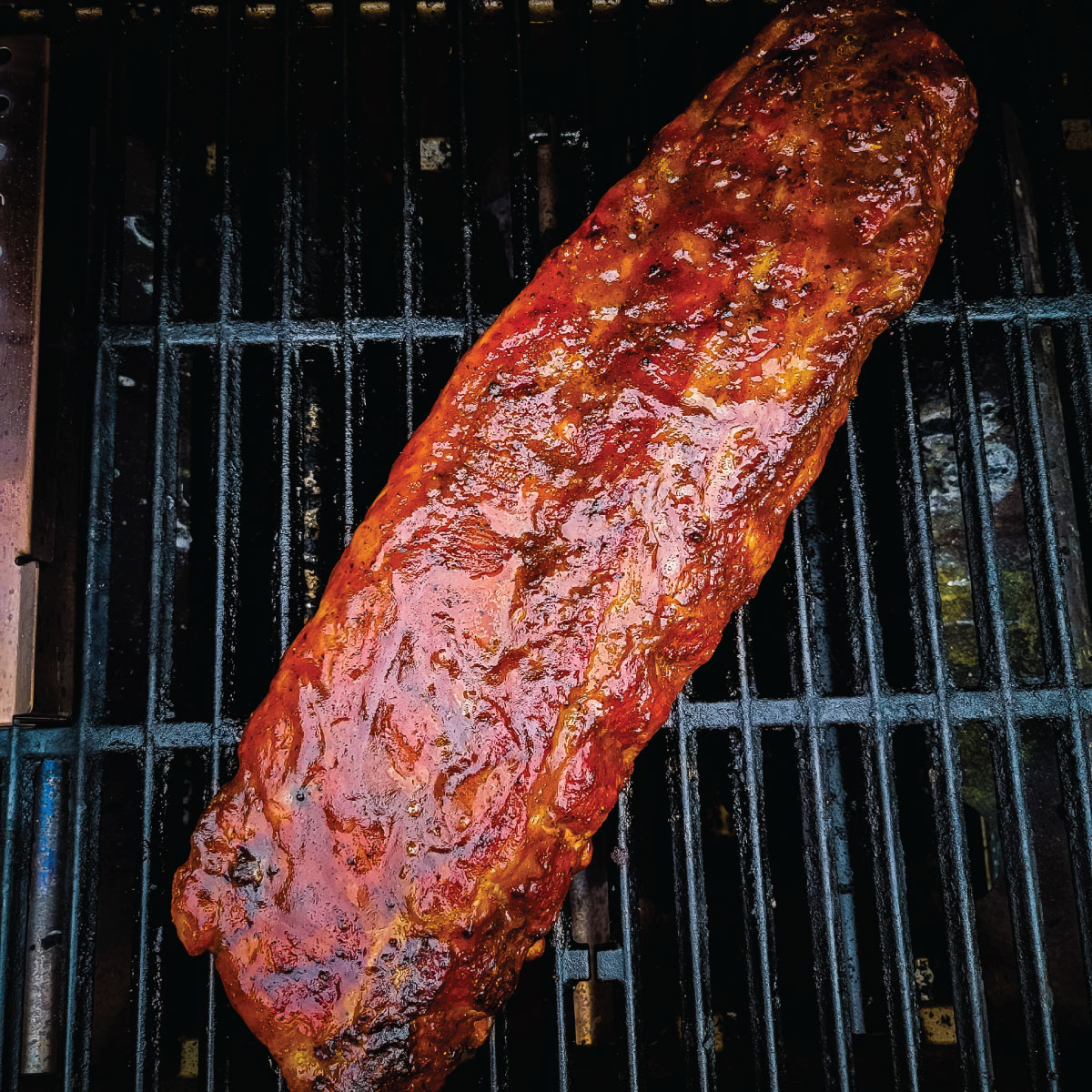 Ribs cooking on the grill with BBQ sauce on them.