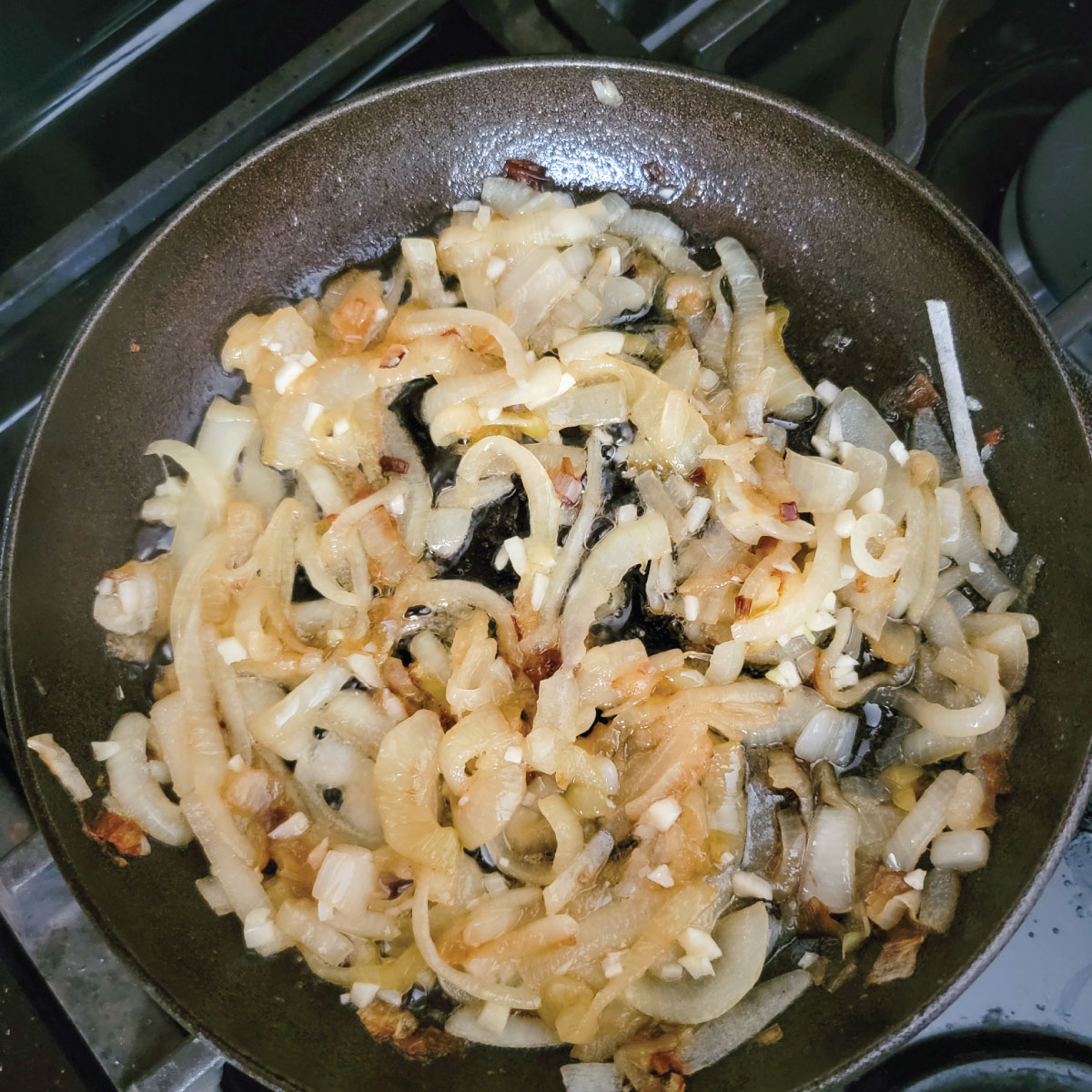 Onions and garlic frying in a pan with butter and oil, the onions are slightly browning