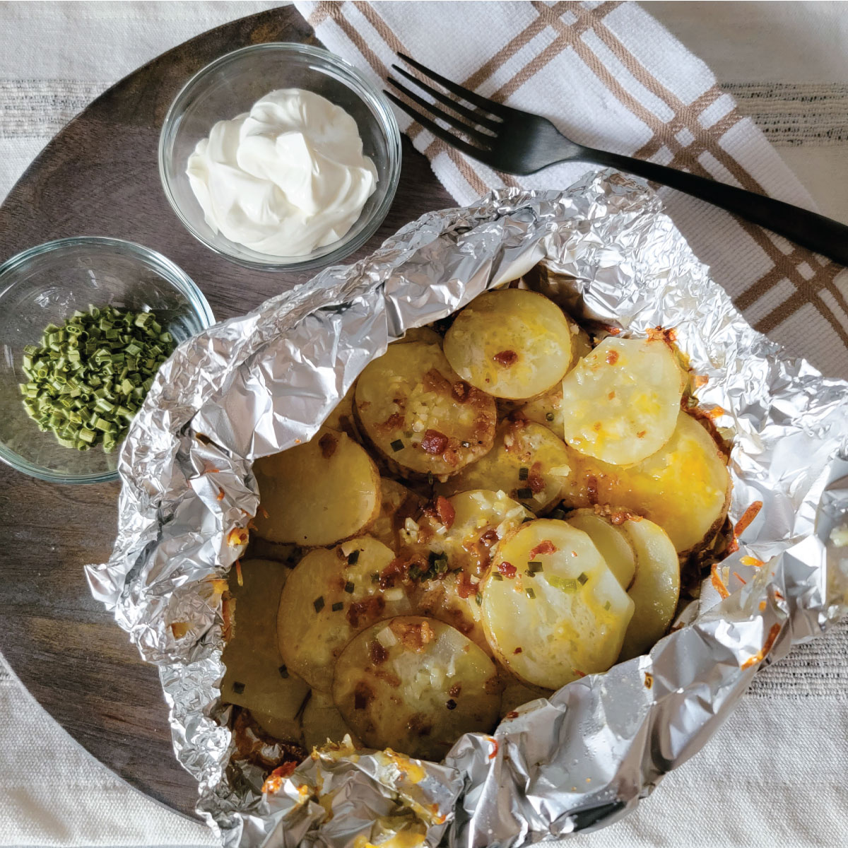 Potatoes in foil on a serving dish topped with bacon, cheese and chives.