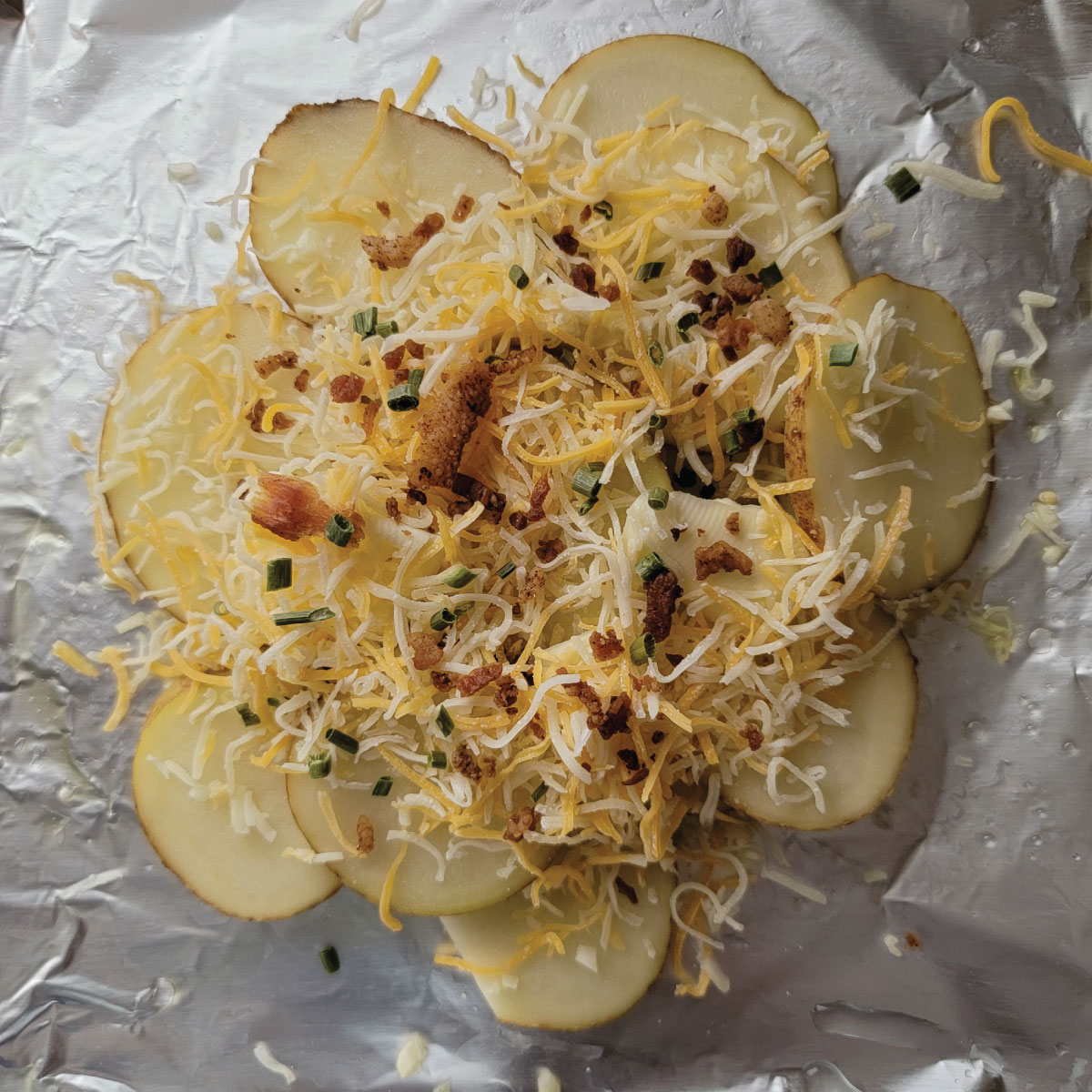 Potato slices on the foil topped with cheese, garlic, chives and bacon.