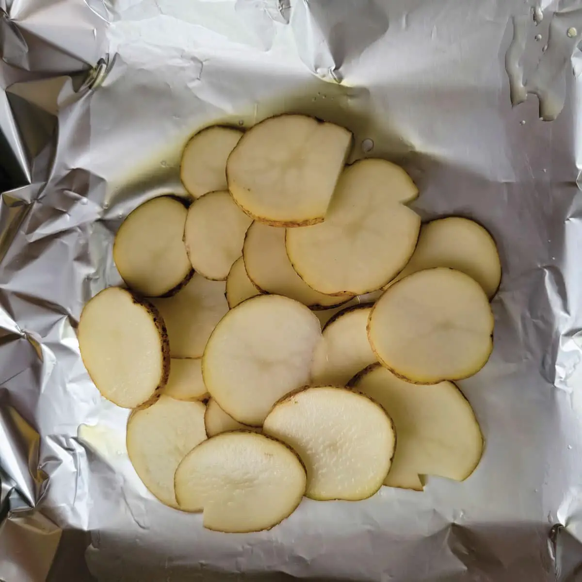 Potatoes on foil after coating foil with olive oil.