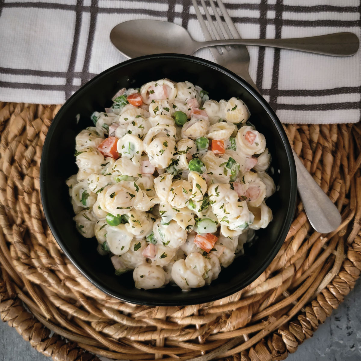 Pasta salad in a bowl with a fork and spoon by the side ready to be eaten