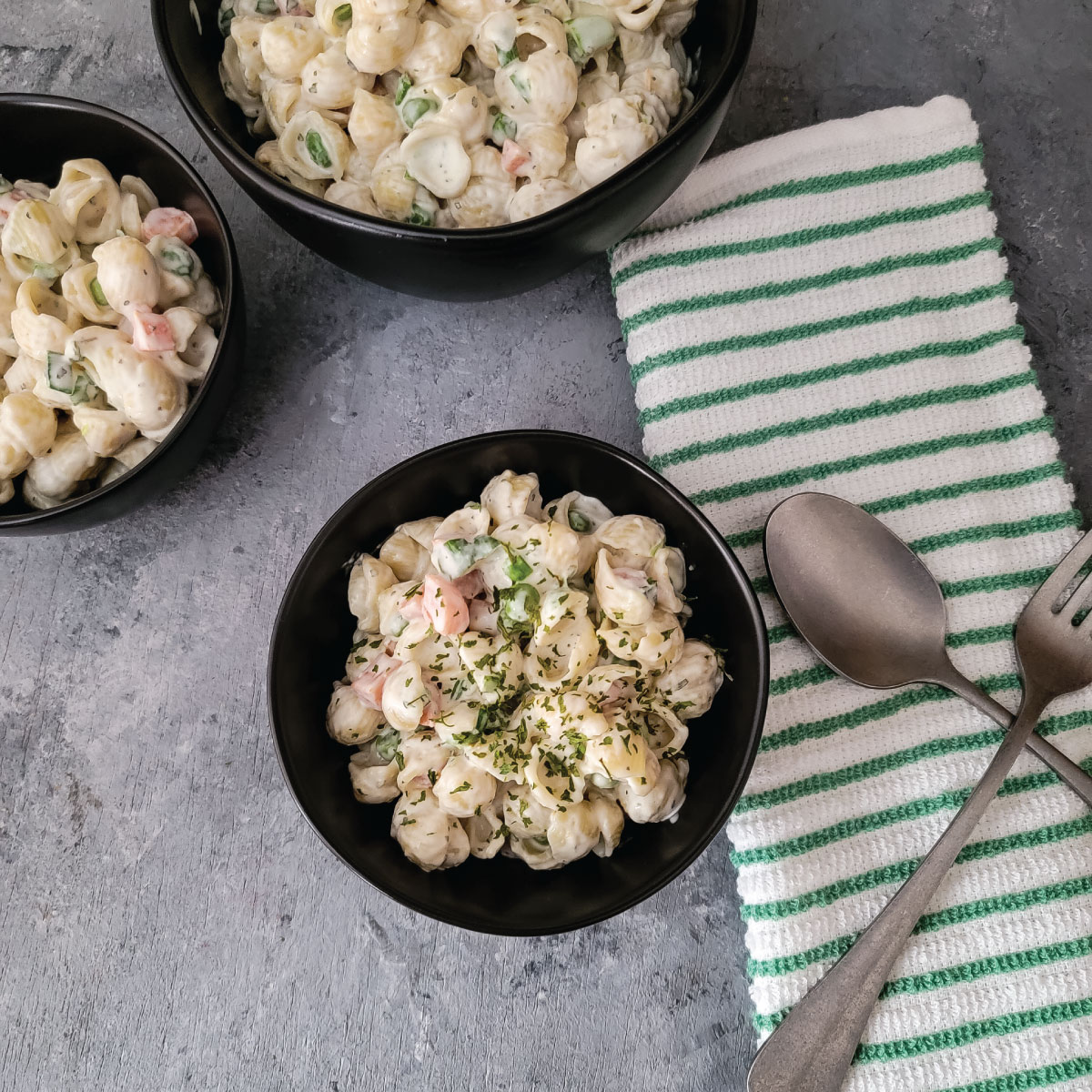 1 larger bowl and 2 smaller bowls with pasta salad in them, 1 is garnished with parsley.  