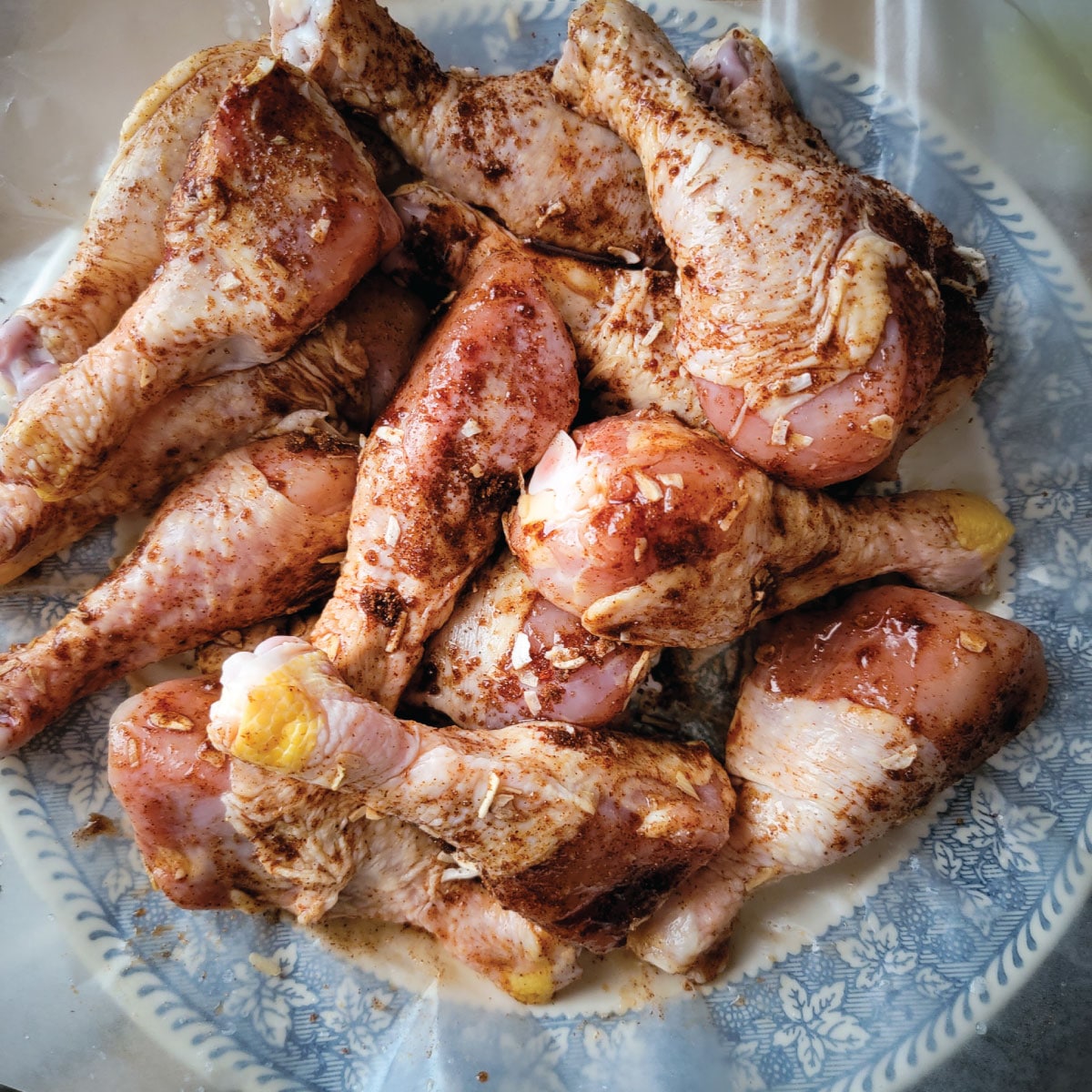 chicken legs on a plate coated with lime juice and dry rub ready for the grill.