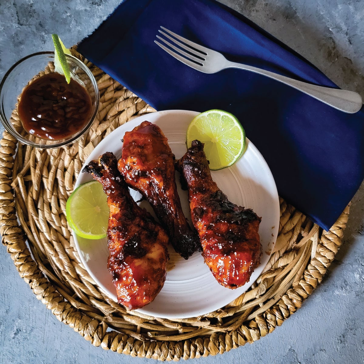 BBQ chicken legs on a plate ready to be served with some extra sauce in a small bowl.