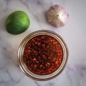 Marinade prepared and sitting in a bowl with a lime and head of garlic as decoration next to it