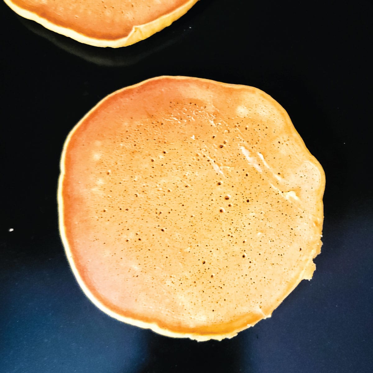 Slightly golden browned pancake on the griddle after being flipped.