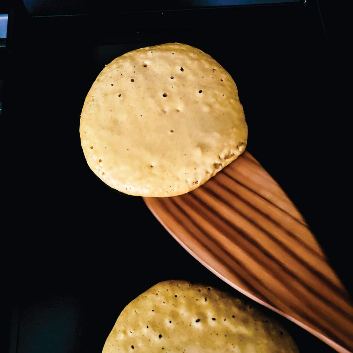 Batter on the griddle with a few bubbles forming in them as they are about to be flipped for the first time.