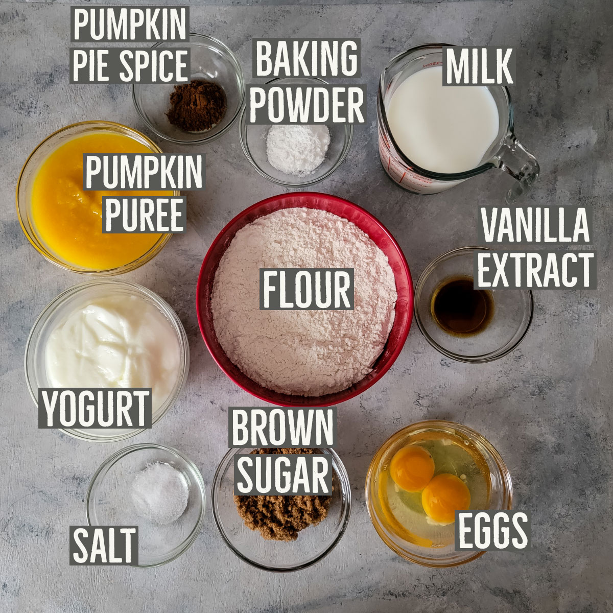 Pumpkin pie spice, baking powder, milk, pumpkin puree, flour, vanilla extract, yogurt, salt, brown sugar and eggs in small prep bowls to display all ingredients.