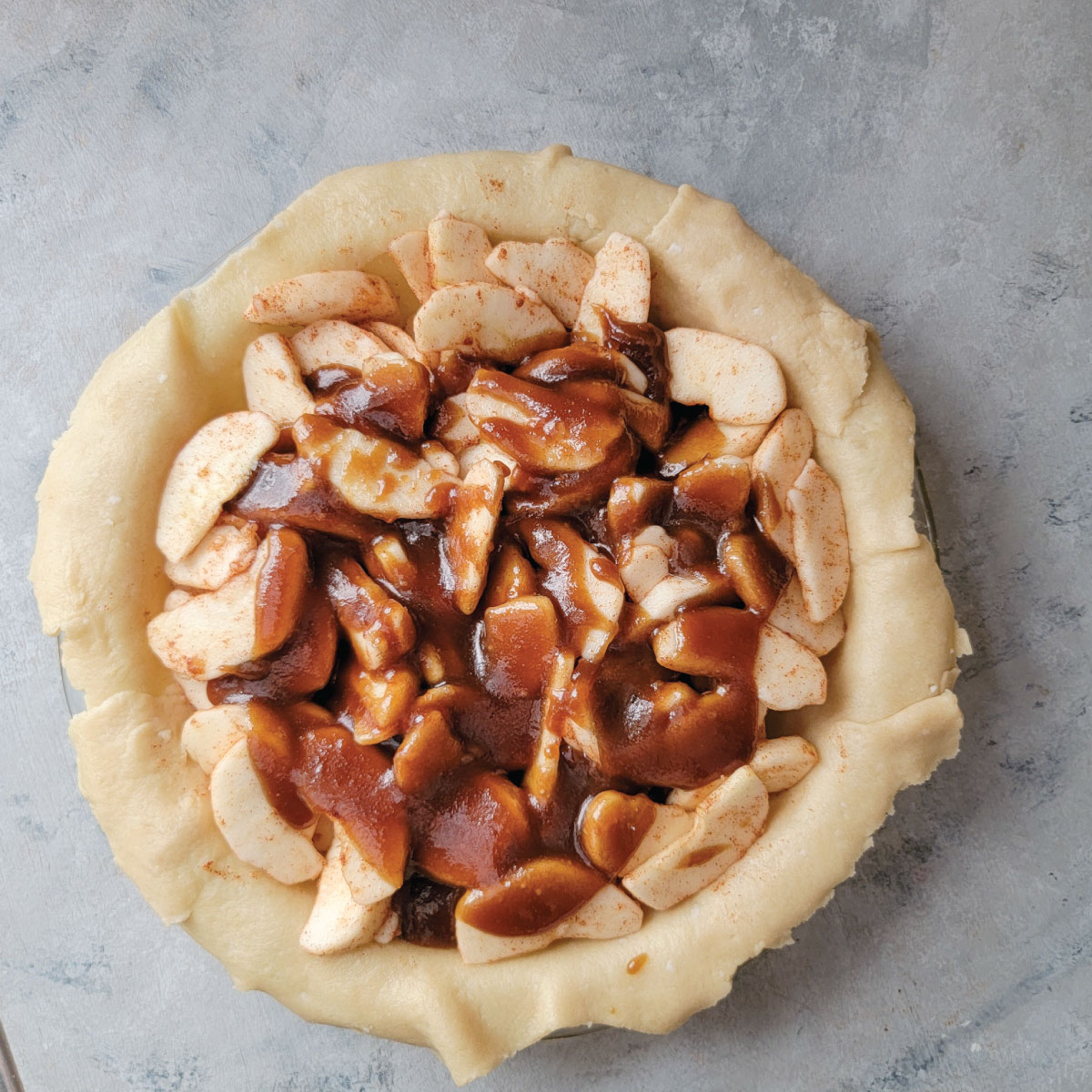 Apples in a pie crust in the pie dish with the sugar sauce poured over top of them.