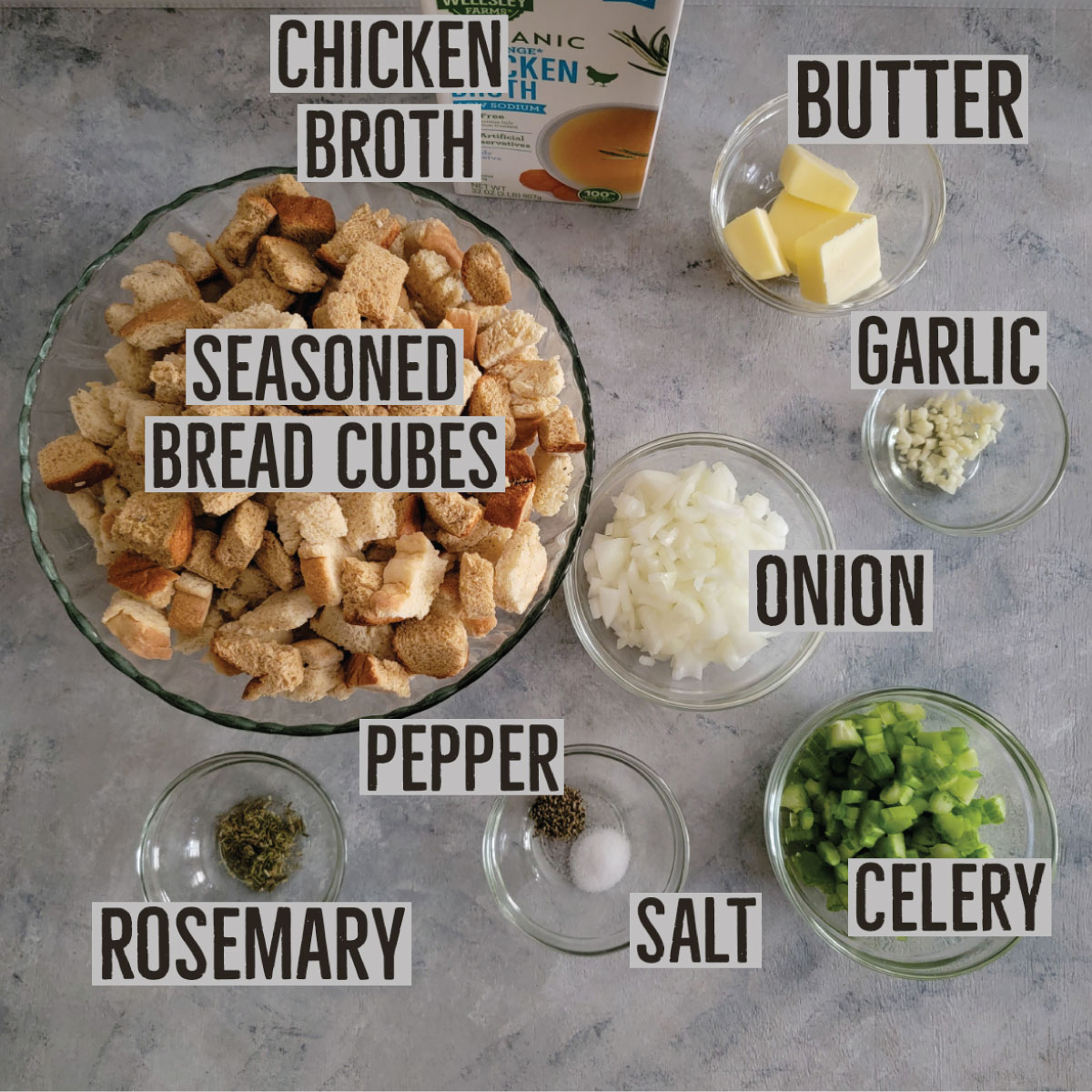 The ingredients prepped for stuffing - seasoned bread cubes, chicken broth, butter, garlic, onion, celery, salt, pepper and rosemary.