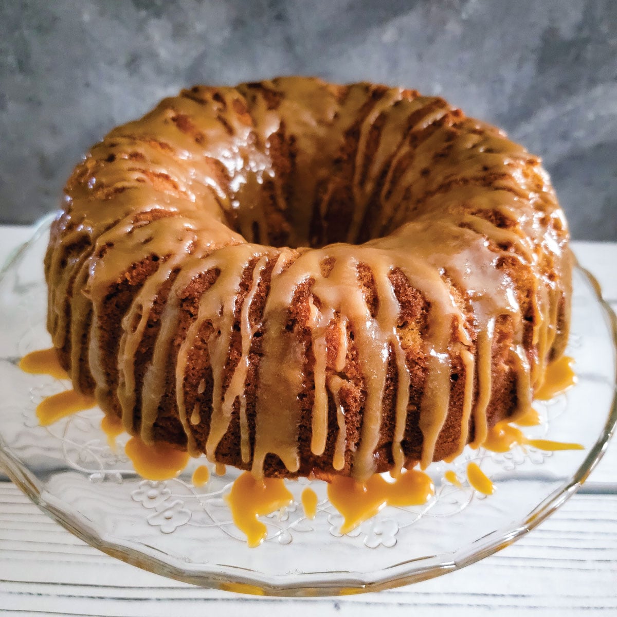 Apple cake with caramel drizzled over the top on a cake platter ready to be served.