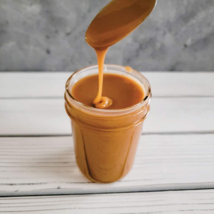 Caramel in a half pint jar with some on a spoon dripping into the jar.