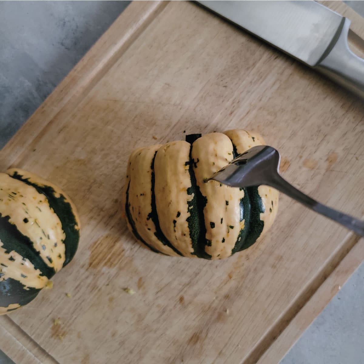 Squash halves skin side up on a cutting board with a fork in one to show poking holes in the skin.