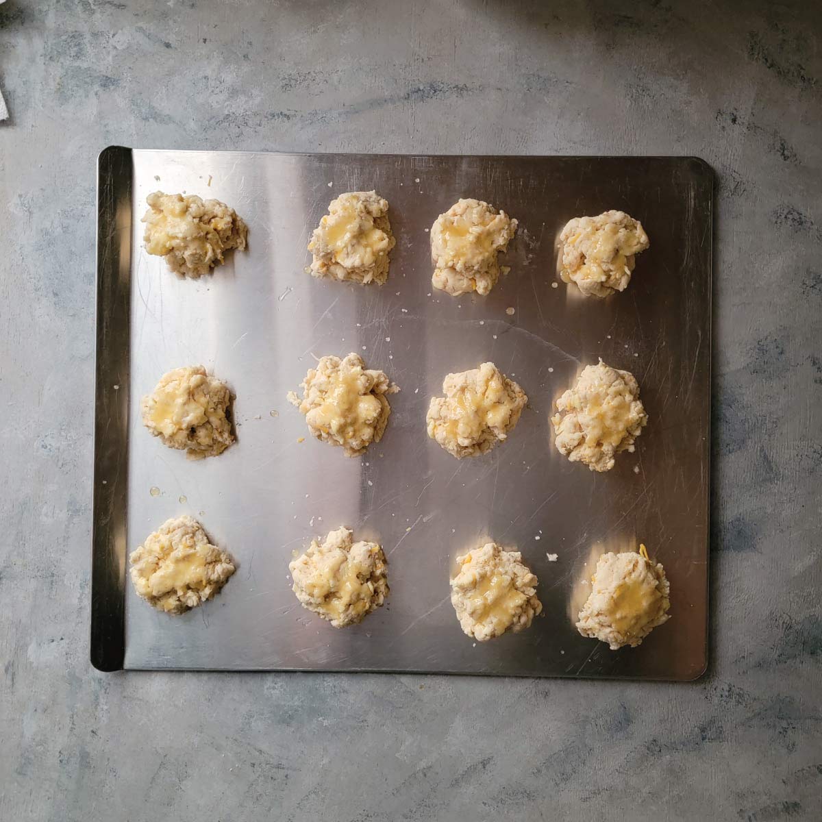 12 biscuits on a baking sheet with melted butter brushed over top just before baking.