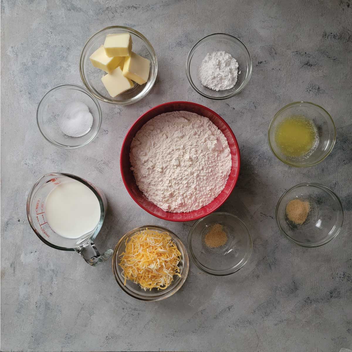 Ingredients prepped - shredded cheese, milk, salt, butter, baking powder, melted butter, garlic powder divided in 2 bowls and flour.