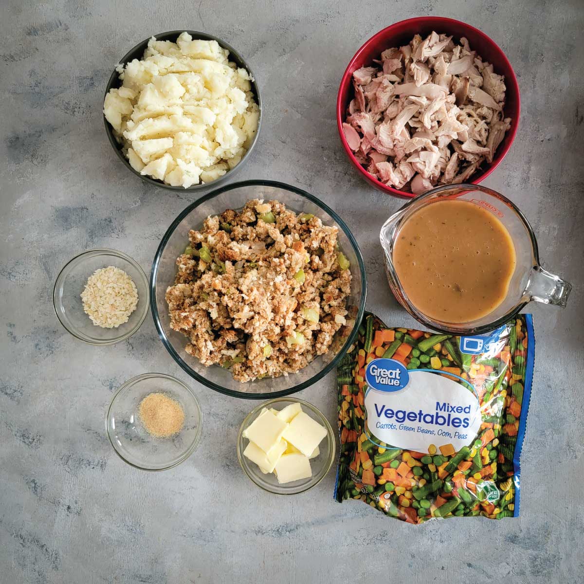 Ingredients for casserole - mixed vegetables, butter, garlic powder, dried minced onion, stuffing, gravy, turkey, and mashed potatoes.
