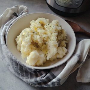Mashed potatoes in a serving bowl with melted butter on top and parsley sprinkled over for a garnish.