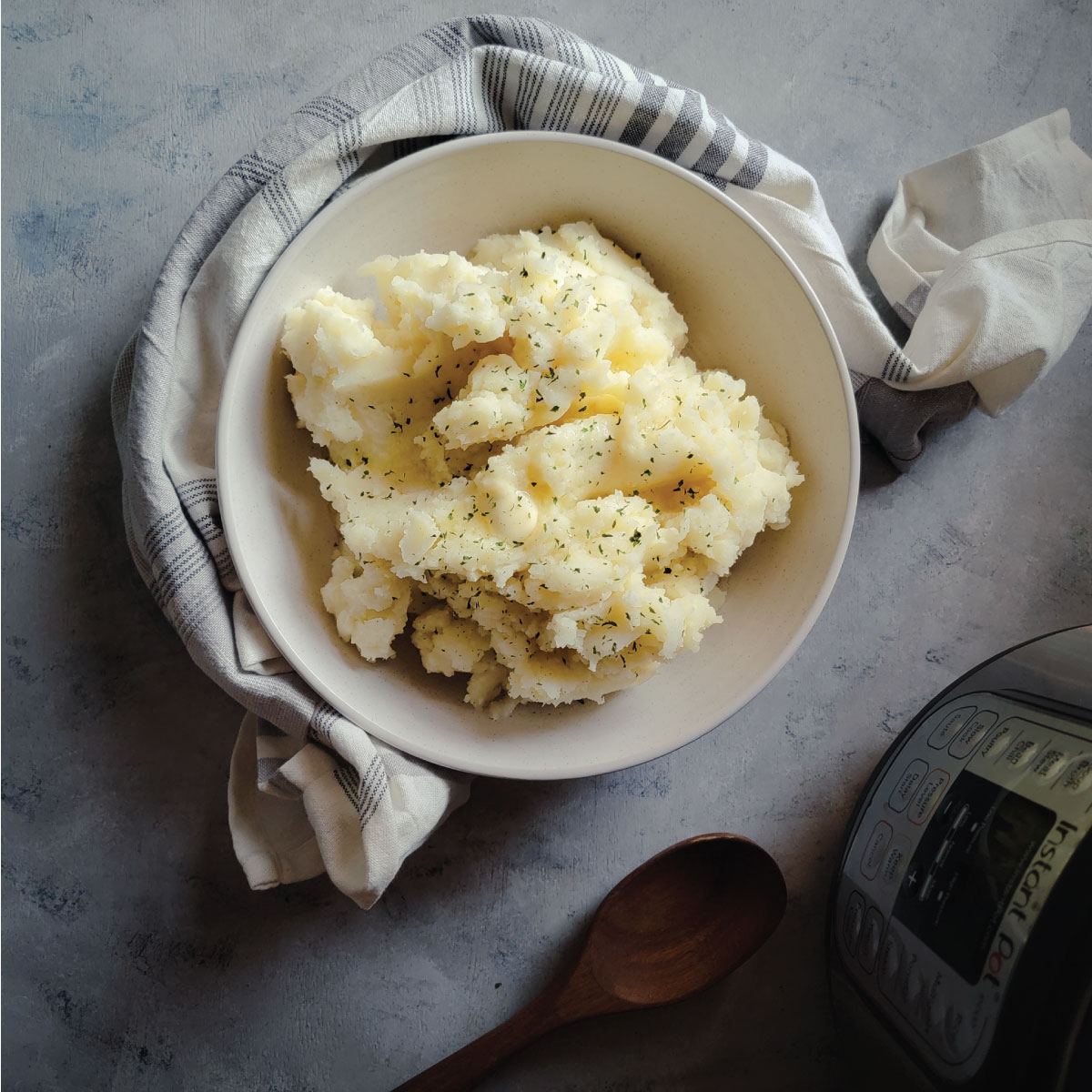 Mashed potatoes in a serving bowl with melted butter on top and parsley sprinkled over for a garnish.