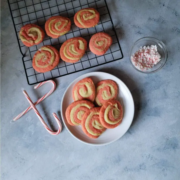 Peppermint pinwheel cookies on a plate and some on a cooling rack with candy canes for decoration.
