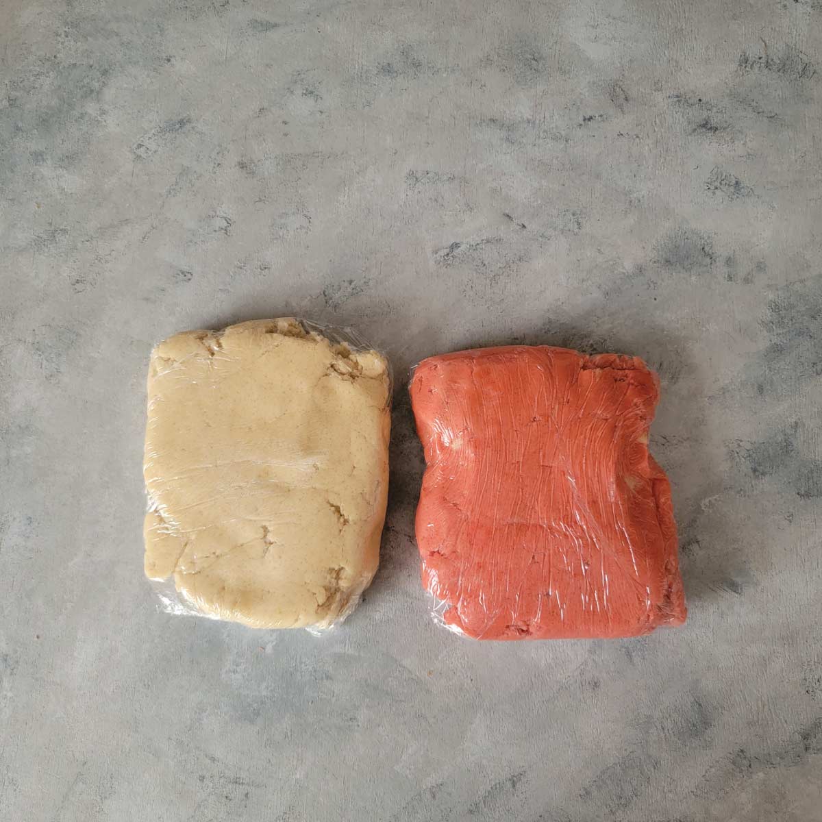 Pink cookie dough and regular cookie dough wrapped separately in plastic wrap.