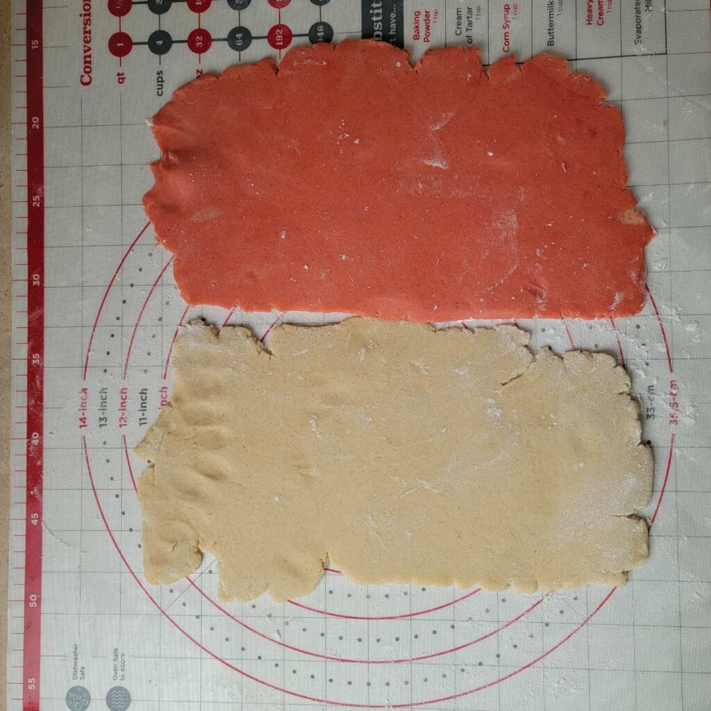 Pink and regular cookie dough rolled out into rectangles close in size with imperfect edges.