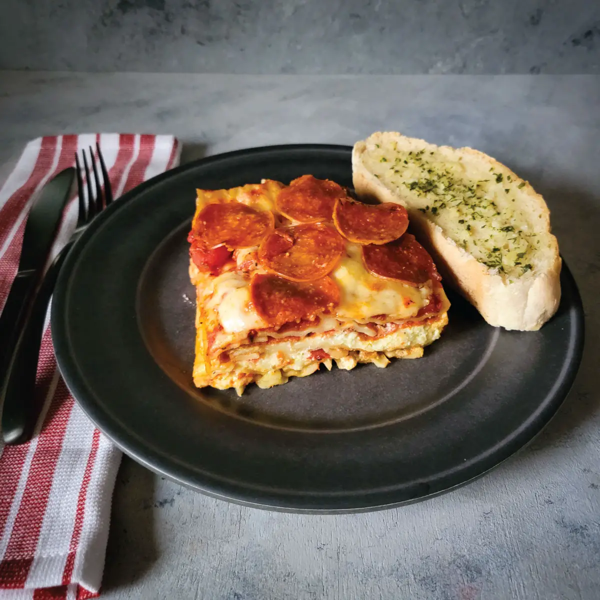Piece of pizza lasagna on a dinner plate with a slice of garlic bread.