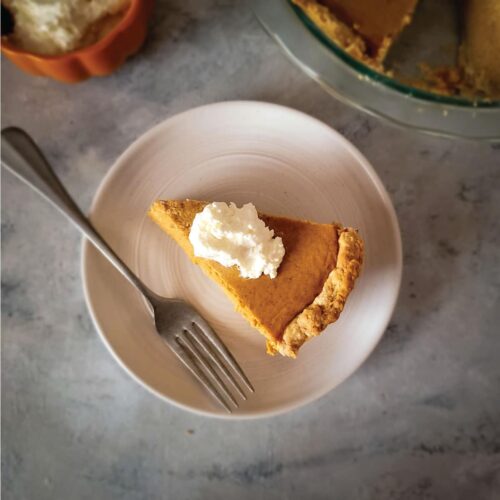 Slice of pumpkin pie on a plate topped with whipped cream ready to serve.